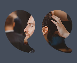 Young man with stylish hair and a full groomed beard in a salon with a stylist holding clippers behind him